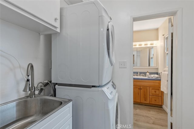 clothes washing area featuring stacked washer and dryer, sink, cabinets, and light hardwood / wood-style floors