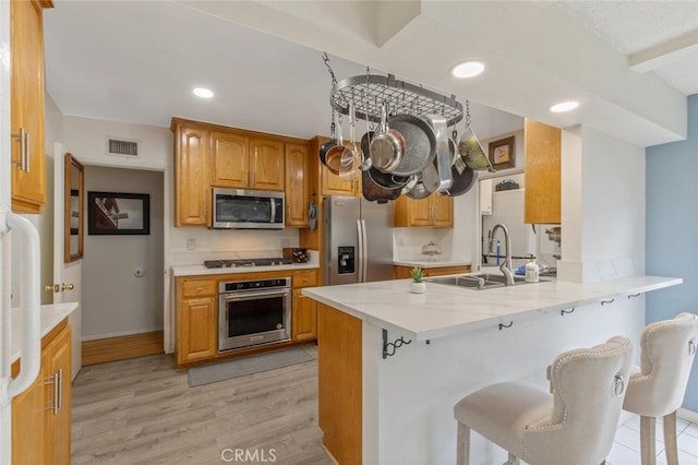 kitchen with sink, light hardwood / wood-style flooring, a breakfast bar, appliances with stainless steel finishes, and kitchen peninsula