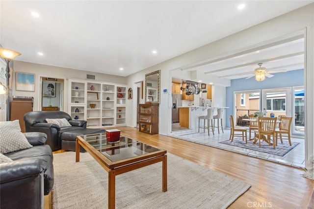 living room featuring beamed ceiling, ceiling fan, and light hardwood / wood-style floors