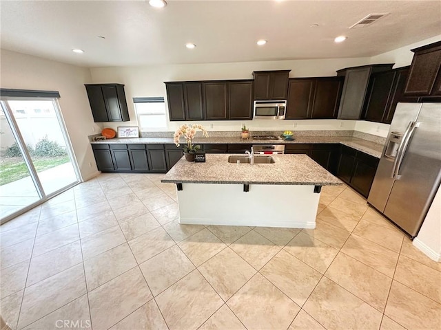 kitchen with sink, a breakfast bar, appliances with stainless steel finishes, light stone countertops, and a center island with sink