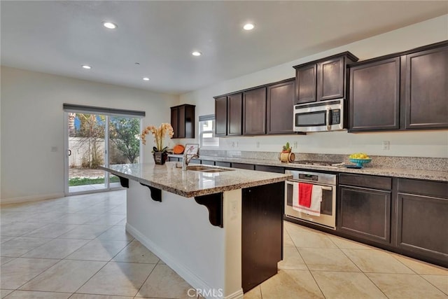 kitchen featuring appliances with stainless steel finishes, sink, light stone countertops, and a kitchen island with sink