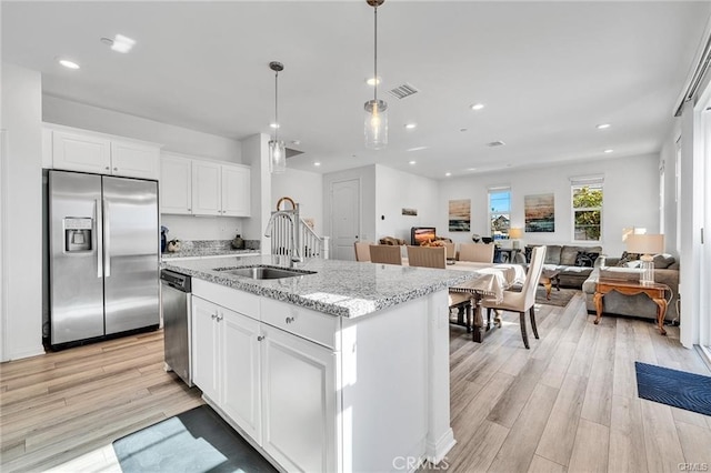 kitchen with decorative light fixtures, white cabinetry, an island with sink, sink, and stainless steel appliances