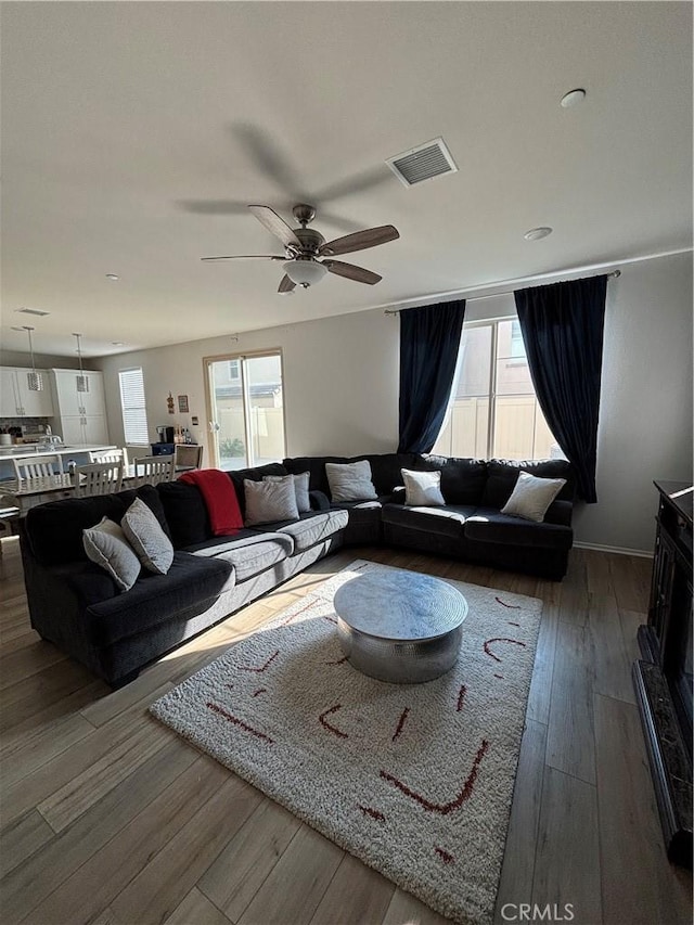 living room featuring dark wood-type flooring, ceiling fan, and plenty of natural light