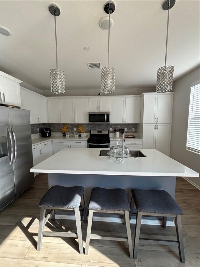 kitchen with decorative light fixtures, white cabinetry, a breakfast bar area, stainless steel appliances, and a center island with sink