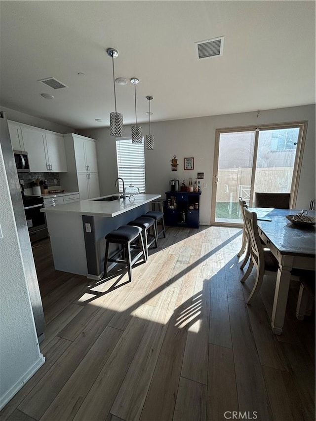 kitchen featuring pendant lighting, a kitchen breakfast bar, white cabinets, a center island with sink, and dark hardwood / wood-style flooring