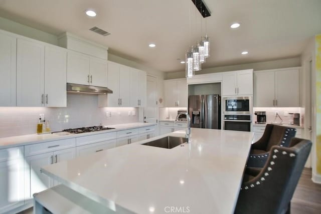 kitchen with sink, decorative light fixtures, a center island with sink, stainless steel appliances, and white cabinets