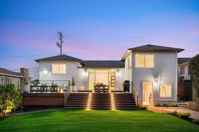 back house at dusk with a wooden deck and a lawn