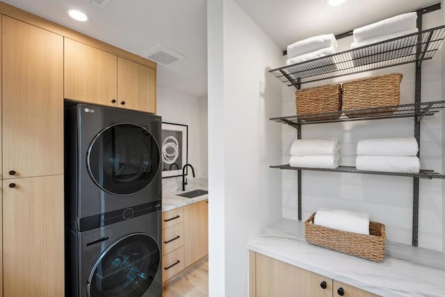 laundry area featuring cabinets, stacked washer / drying machine, sink, and light wood-type flooring