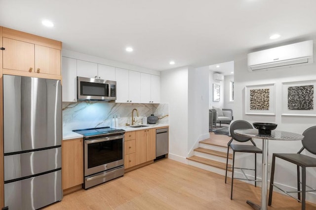 kitchen featuring appliances with stainless steel finishes, white cabinetry, sink, a wall unit AC, and light hardwood / wood-style flooring