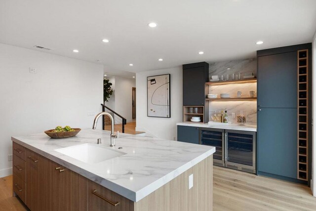 bar with light stone counters, beverage cooler, sink, and light wood-type flooring