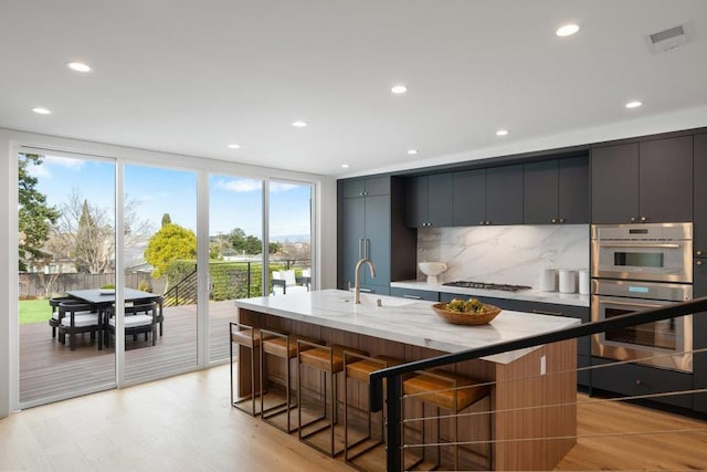 kitchen featuring a breakfast bar, an island with sink, sink, backsplash, and light hardwood / wood-style floors