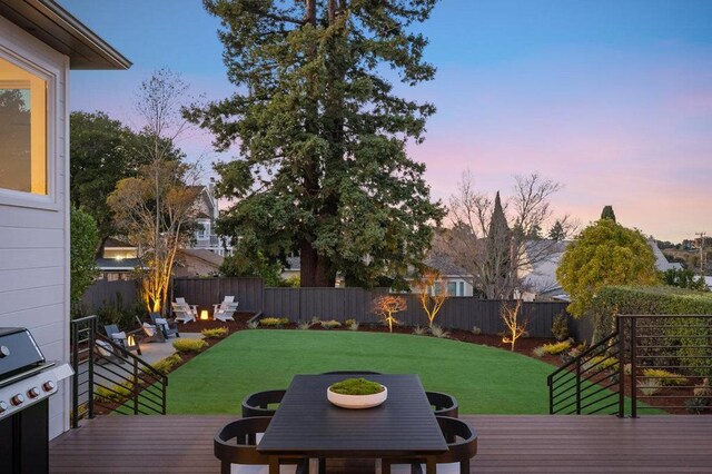 deck at dusk featuring a grill and a lawn