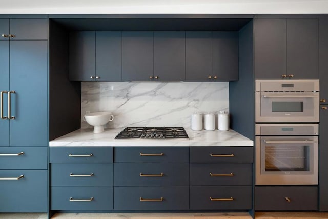 kitchen with stainless steel gas stovetop, light stone counters, backsplash, and double oven