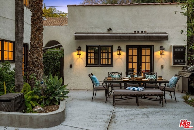 back house at dusk featuring french doors and a patio area