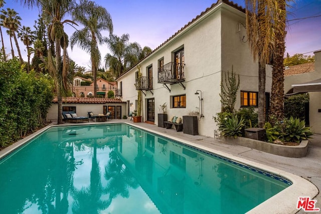 pool at dusk featuring cooling unit and a patio