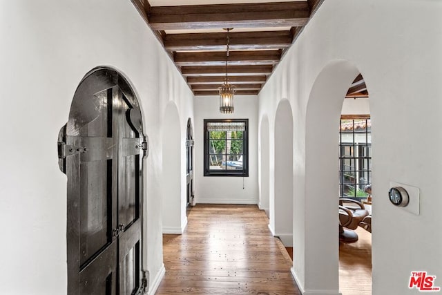 hall with a notable chandelier, beam ceiling, and light wood-type flooring