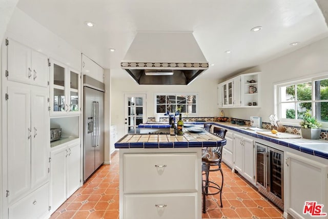 kitchen with stainless steel built in refrigerator, a breakfast bar, tile counters, and white cabinets