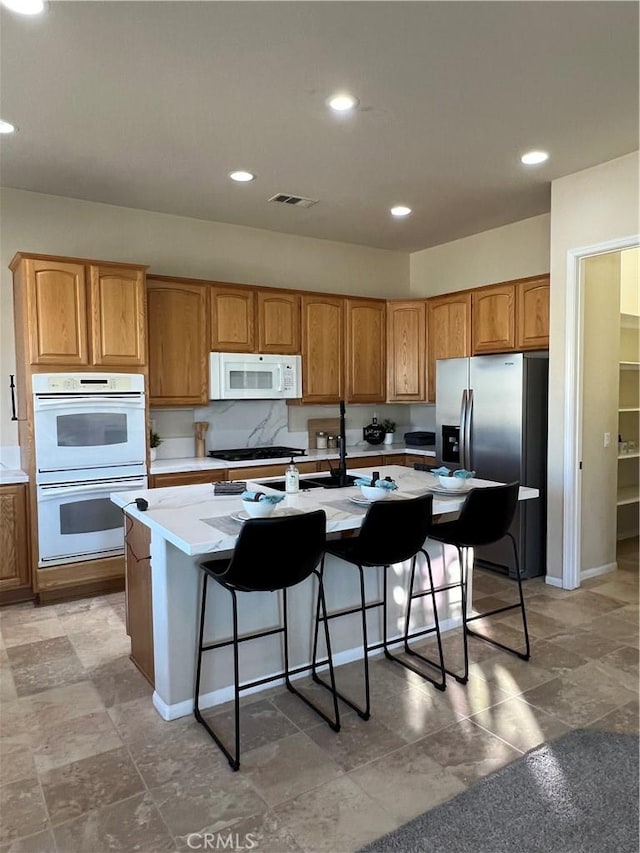 kitchen featuring white appliances, a breakfast bar area, and an island with sink