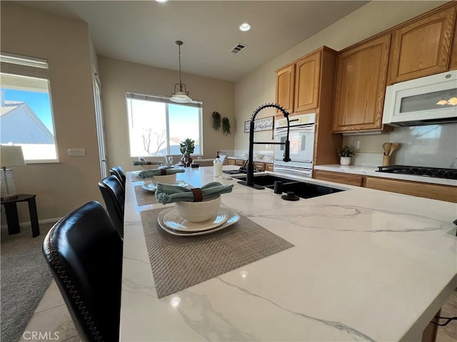 kitchen with sink, a breakfast bar area, hanging light fixtures, gas cooktop, and light stone countertops