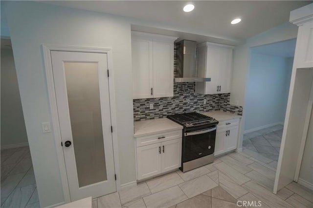 kitchen featuring white cabinetry, decorative backsplash, light stone countertops, stainless steel gas stove, and wall chimney exhaust hood