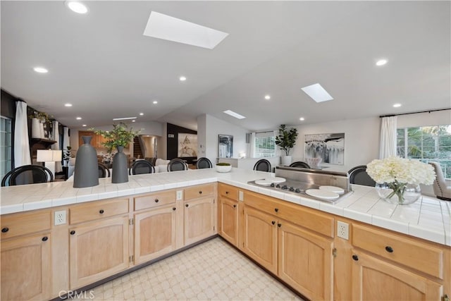 kitchen featuring lofted ceiling with skylight, tile counters, light brown cabinetry, and kitchen peninsula