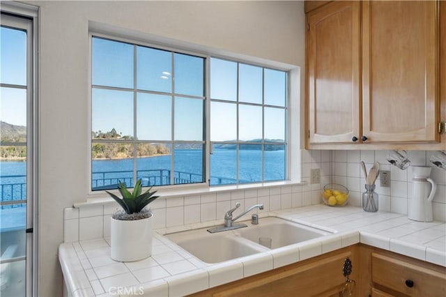 kitchen with tasteful backsplash, a water view, sink, and tile countertops