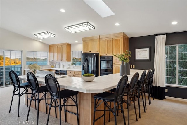 kitchen with lofted ceiling with skylight, tile countertops, light brown cabinetry, black refrigerator with ice dispenser, and light colored carpet