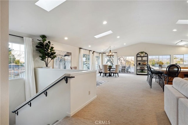 carpeted living room with plenty of natural light, vaulted ceiling with skylight, and a notable chandelier