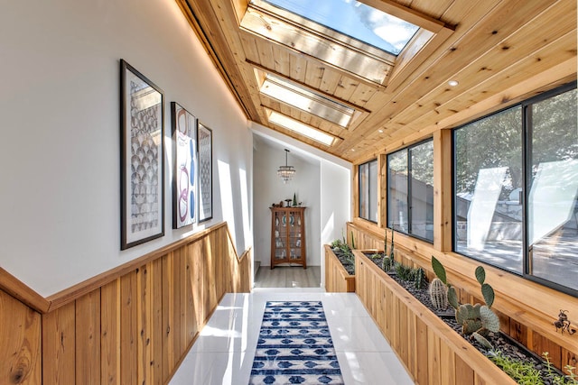 hall featuring wooden walls, vaulted ceiling with skylight, and wood ceiling