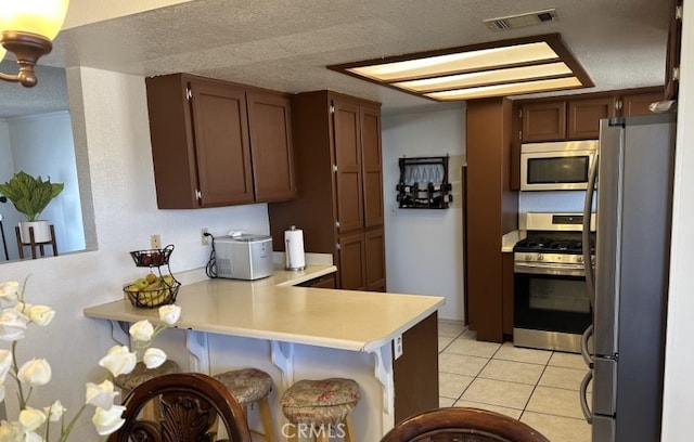 kitchen with light tile patterned floors, a breakfast bar area, appliances with stainless steel finishes, a textured ceiling, and kitchen peninsula