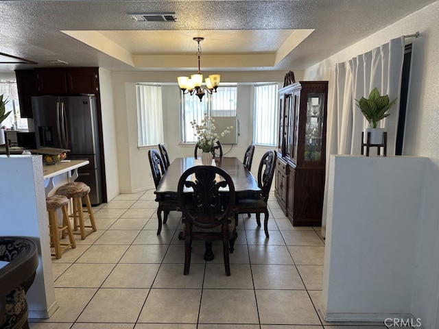 tiled dining room featuring a textured ceiling, an inviting chandelier, and a tray ceiling