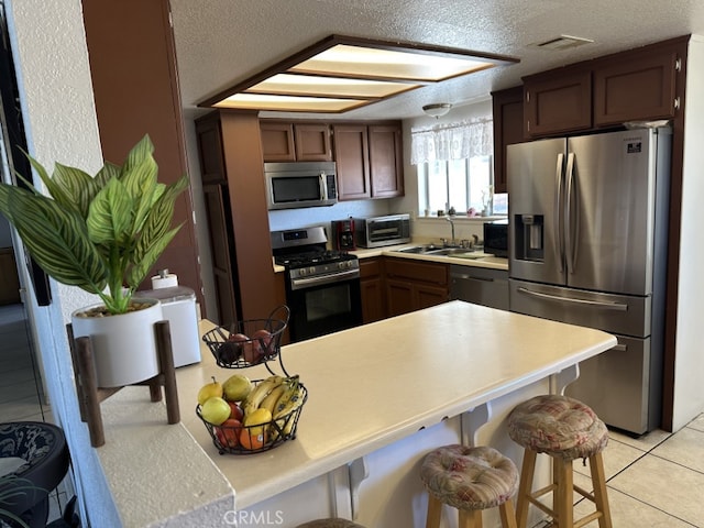 kitchen featuring sink, a breakfast bar, stainless steel appliances, a textured ceiling, and light tile patterned flooring