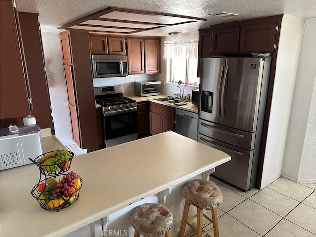 kitchen with sink, appliances with stainless steel finishes, a textured ceiling, a kitchen bar, and light tile patterned flooring