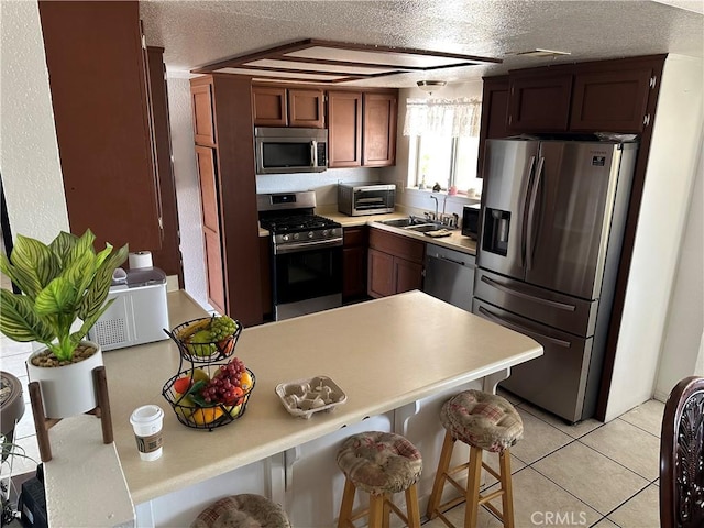 kitchen featuring light tile patterned flooring, a kitchen bar, sink, a textured ceiling, and appliances with stainless steel finishes