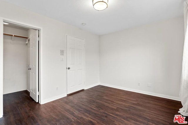 unfurnished bedroom featuring a walk in closet, dark wood-type flooring, and a closet