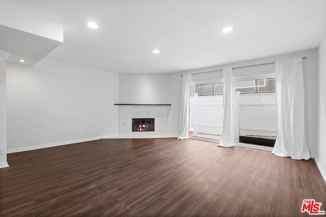 unfurnished living room featuring a brick fireplace and dark wood-type flooring