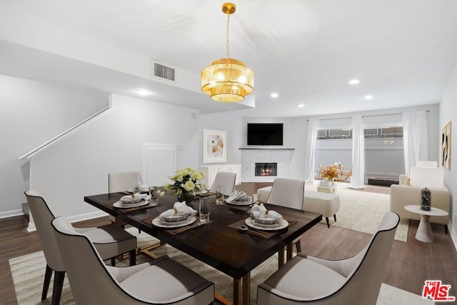 dining space featuring hardwood / wood-style flooring, a brick fireplace, and a chandelier