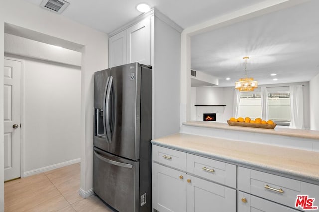 kitchen with white cabinetry, stainless steel refrigerator with ice dispenser, light tile patterned floors, and decorative light fixtures