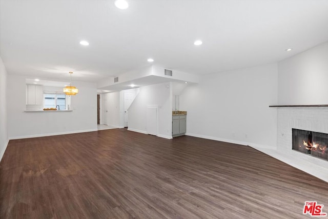 unfurnished living room with a brick fireplace, dark wood-type flooring, and a notable chandelier