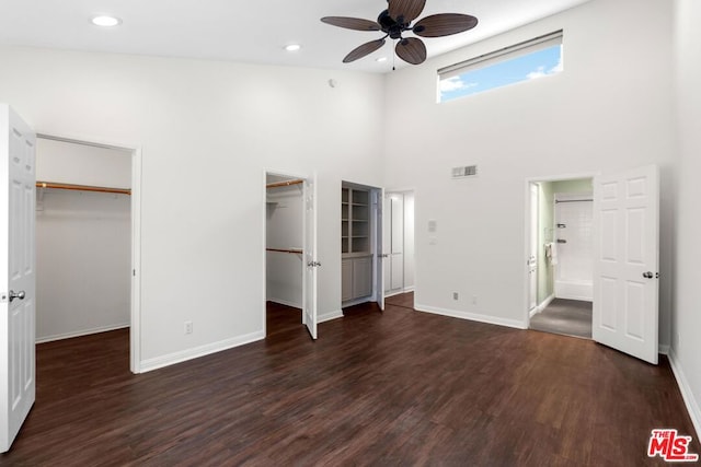 unfurnished bedroom with a walk in closet, ensuite bathroom, dark hardwood / wood-style flooring, and a high ceiling