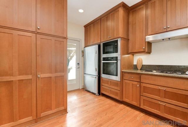 kitchen with stainless steel appliances, light hardwood / wood-style floors, and dark stone countertops