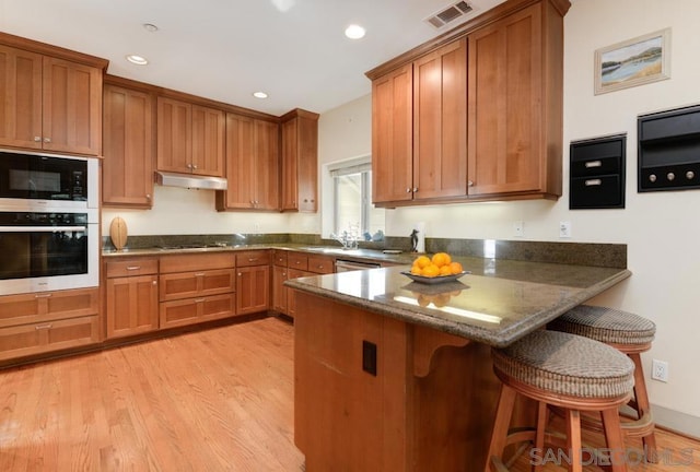 kitchen with light hardwood / wood-style flooring, black appliances, a breakfast bar, and kitchen peninsula