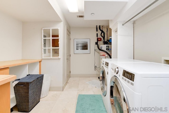 clothes washing area featuring water heater, independent washer and dryer, and light tile patterned flooring