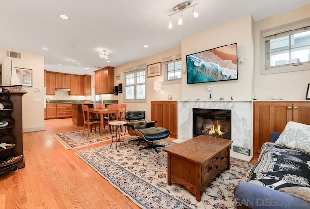 living room with a high end fireplace and light hardwood / wood-style floors