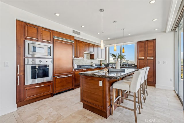 kitchen with visible vents, dark stone counters, a kitchen island, built in appliances, and hanging light fixtures