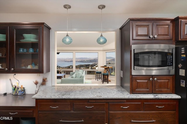 kitchen featuring hanging light fixtures, light stone countertops, black refrigerator, and dark brown cabinets