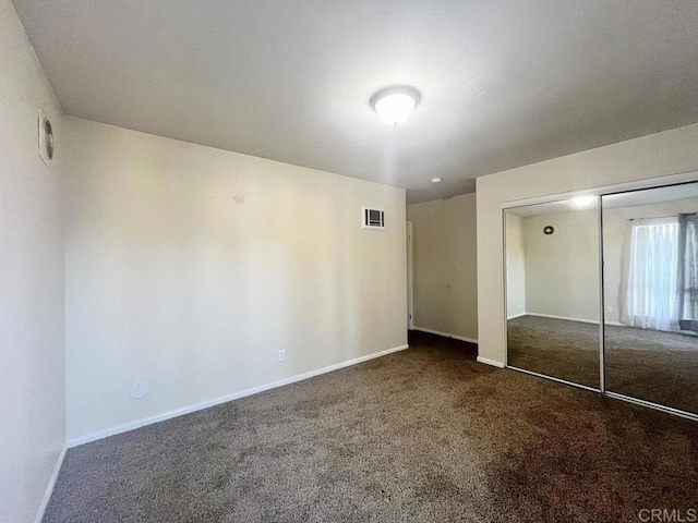 unfurnished bedroom with dark colored carpet and a closet