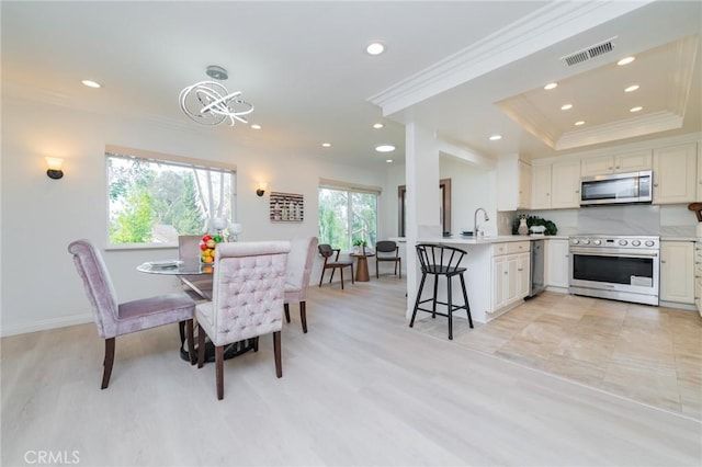 dining space with ornamental molding, a tray ceiling, and sink