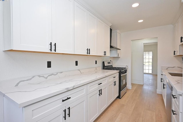 kitchen with light hardwood / wood-style flooring, appliances with stainless steel finishes, white cabinets, light stone countertops, and wall chimney range hood