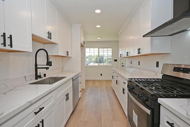 kitchen with sink, stainless steel appliances, light stone counters, white cabinets, and wall chimney exhaust hood